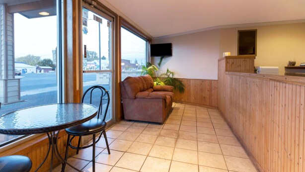 A hotel room with a large window, a sofa, a small table with chairs, and a television mounted on the wall. - Knights Inn Baker City (Baker City)