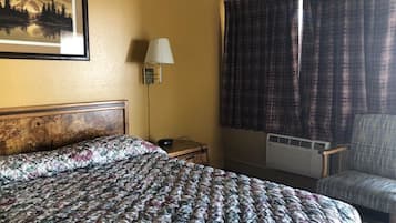 A hotel room with a large bed, a desk with a lamp, a chair, and a window with curtains.