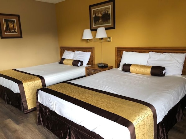 A hotel room with two beds, each with a white and brown bedspread, and a wall-mounted lamp.