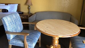 A hotel room with a bed, a round wooden table, two blue plaid chairs, a lamp, and a sofa. - Knights Inn Baker City (Baker City)