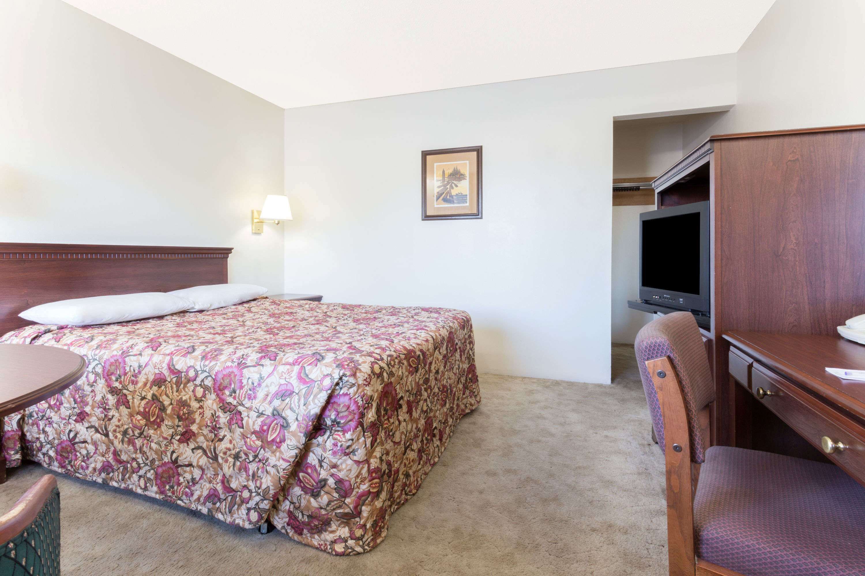 Een hotelkamer met een bed, een bureau, een stoel, een televisie en een ingelijst kunstwerk aan de muur.