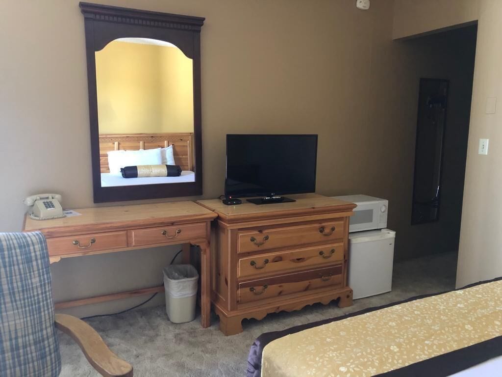 A hotel room with a wooden desk, a television, a dresser, and a bed.