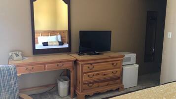 A hotel room with a wooden desk, a television, a dresser, and a bed.