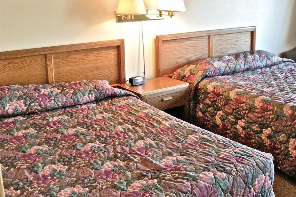 A hotel room with two beds, each with floral-patterned bedding, a nightstand with a lamp, and a framed picture on the wall.