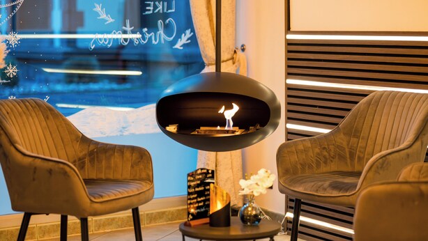 Een modern interieur met twee leren fauteuils, een ronde tafel met een decoratief object, en een bijzondere zwarte hanglamp.