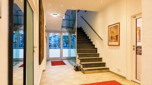 Een moderne hotelentree met een trap, een roodgekleurd tapijt en een grote spiegel.