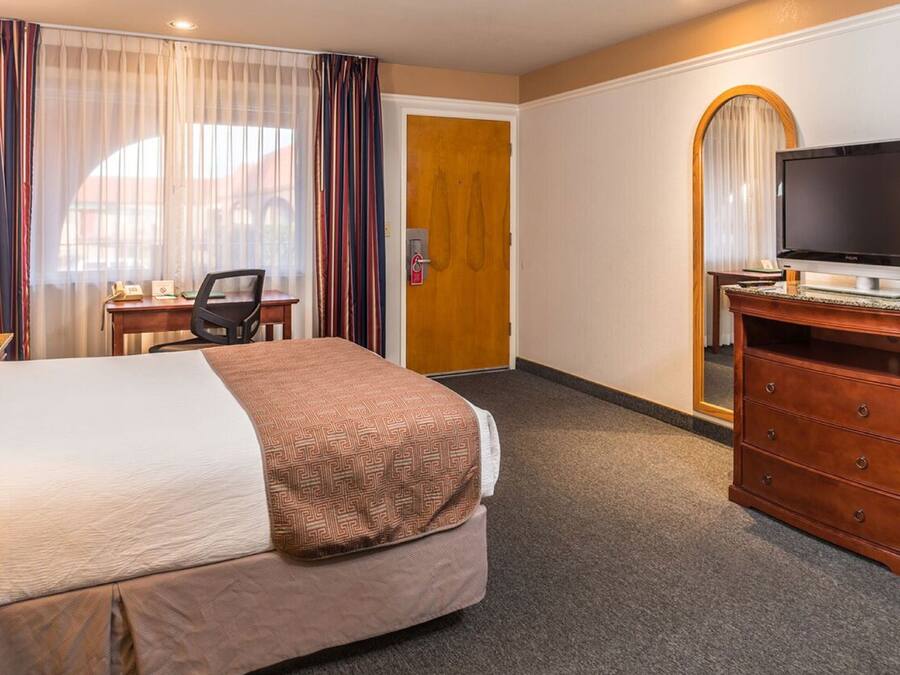 A hotel room with a bed, a desk, a television on a stand, and a door with a mirror.