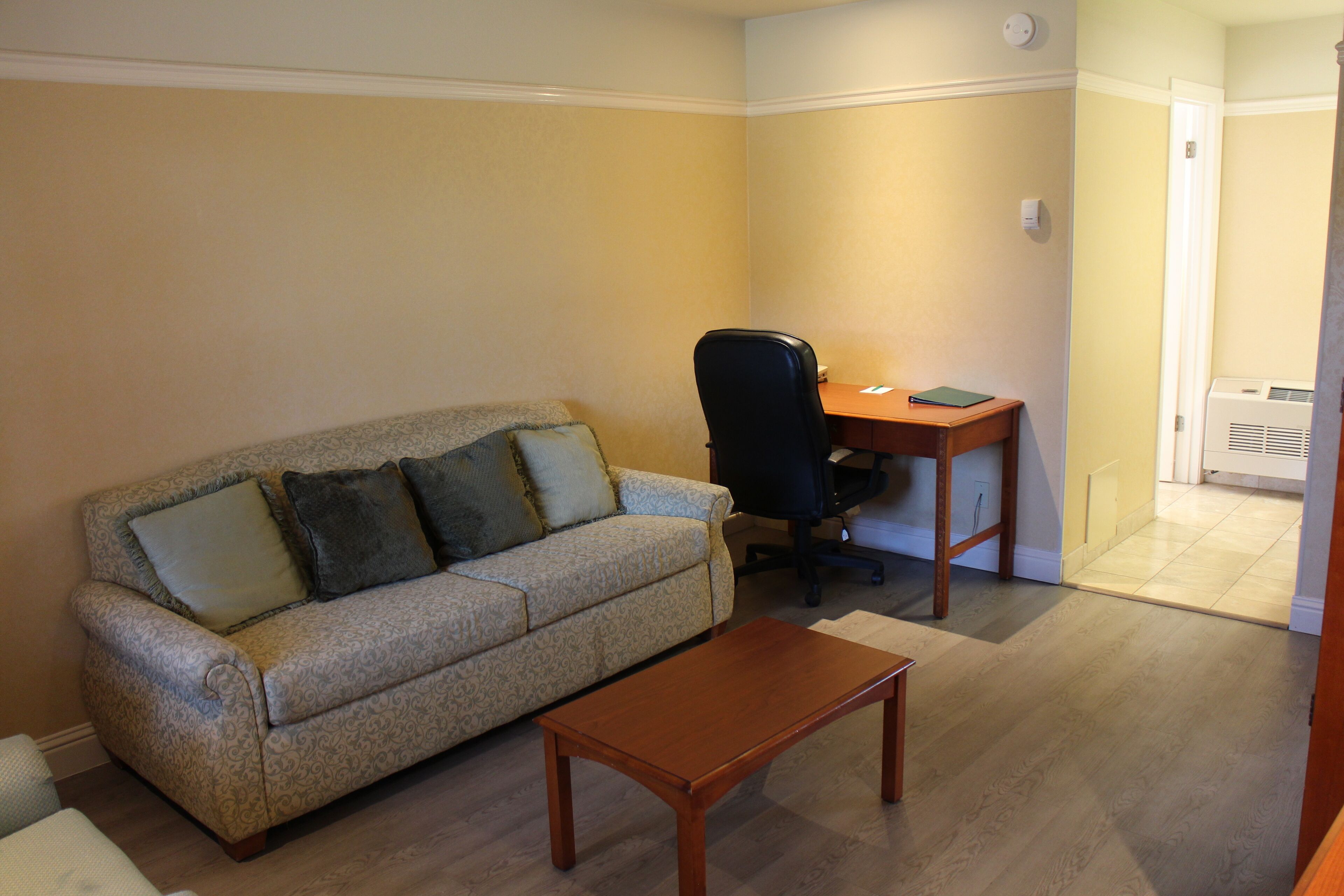 A living room with a sofa, a wooden coffee table, and a desk with a chair.