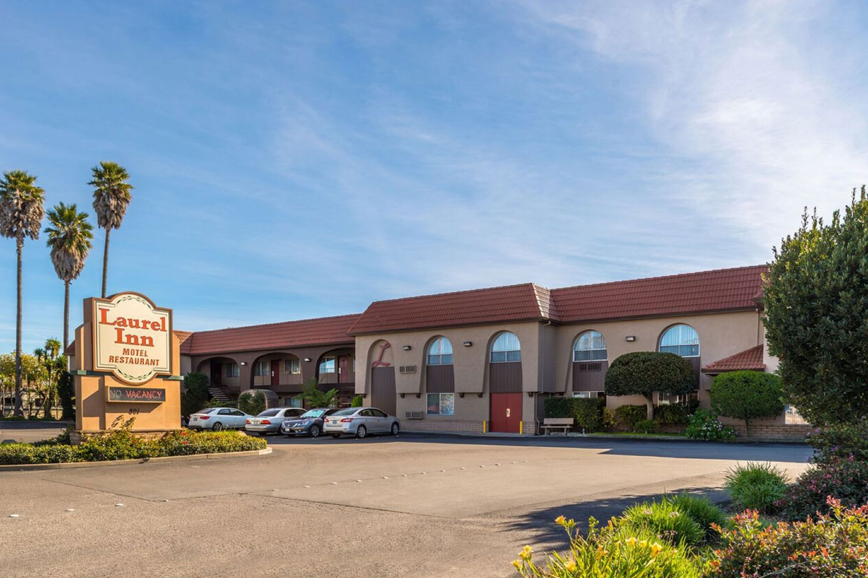 A Laurel Inn Motel and Restaurant with a parking lot, palm trees, and a clear sky.