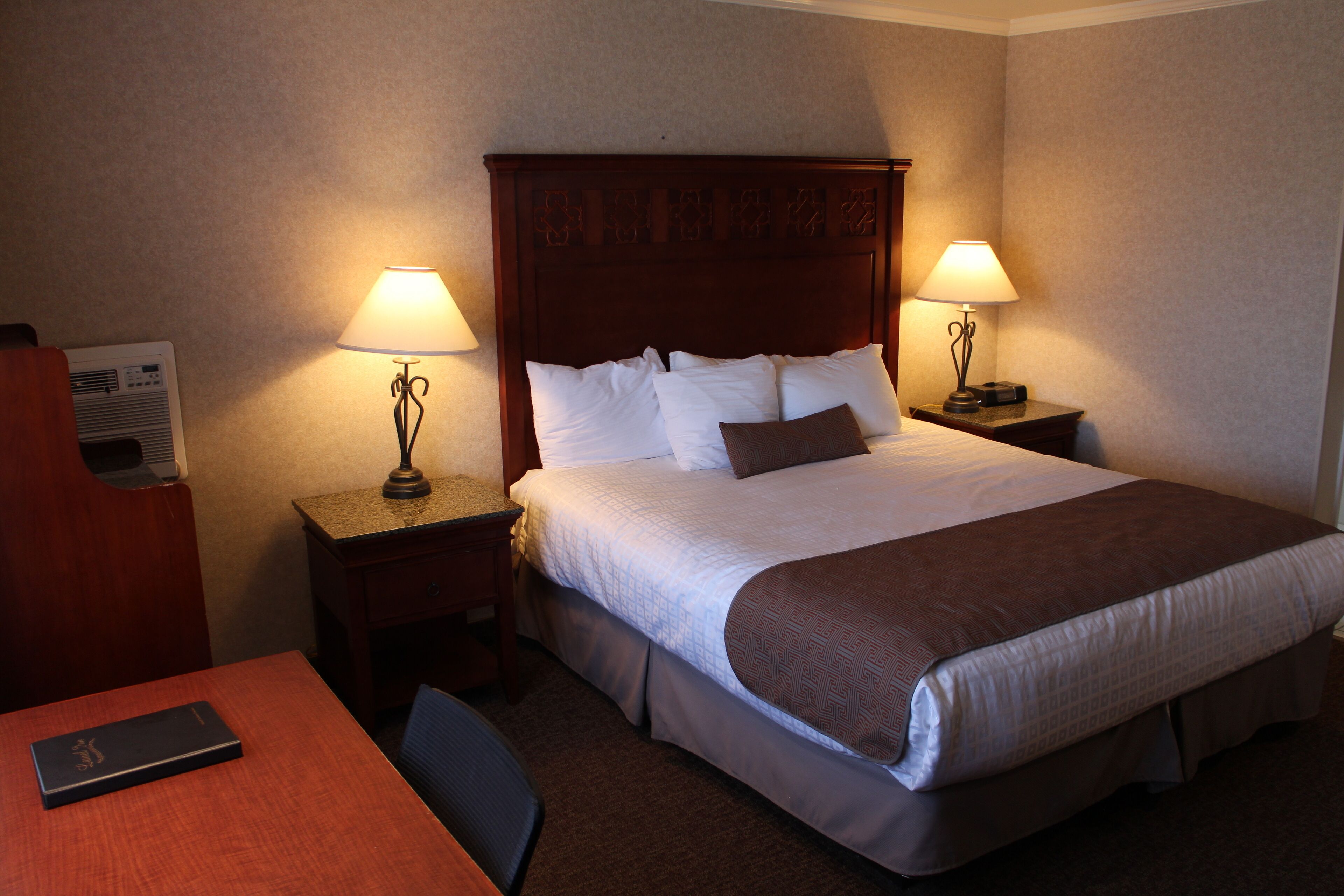A hotel room with a large bed, two bedside tables with lamps, a desk with a chair, and a small table with a telephone.