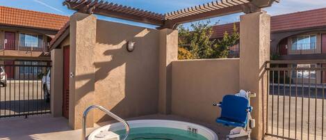Un jacuzzi con una pérgola arriba, una escalera metálica y una silla azul.