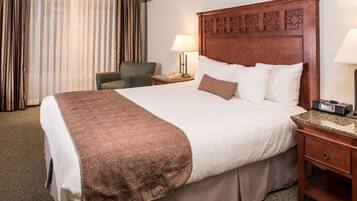 Una habitación de hotel con una cama grande, un cabecero de madera, un escritorio con lámpara, una silla y una ventana con cortinas.