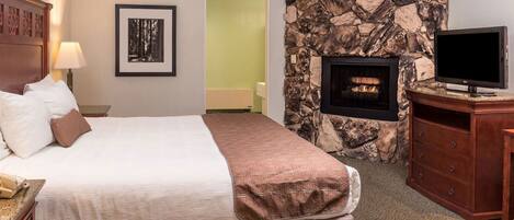 A hotel room with a bed, a television, a fireplace, and a stone wall.