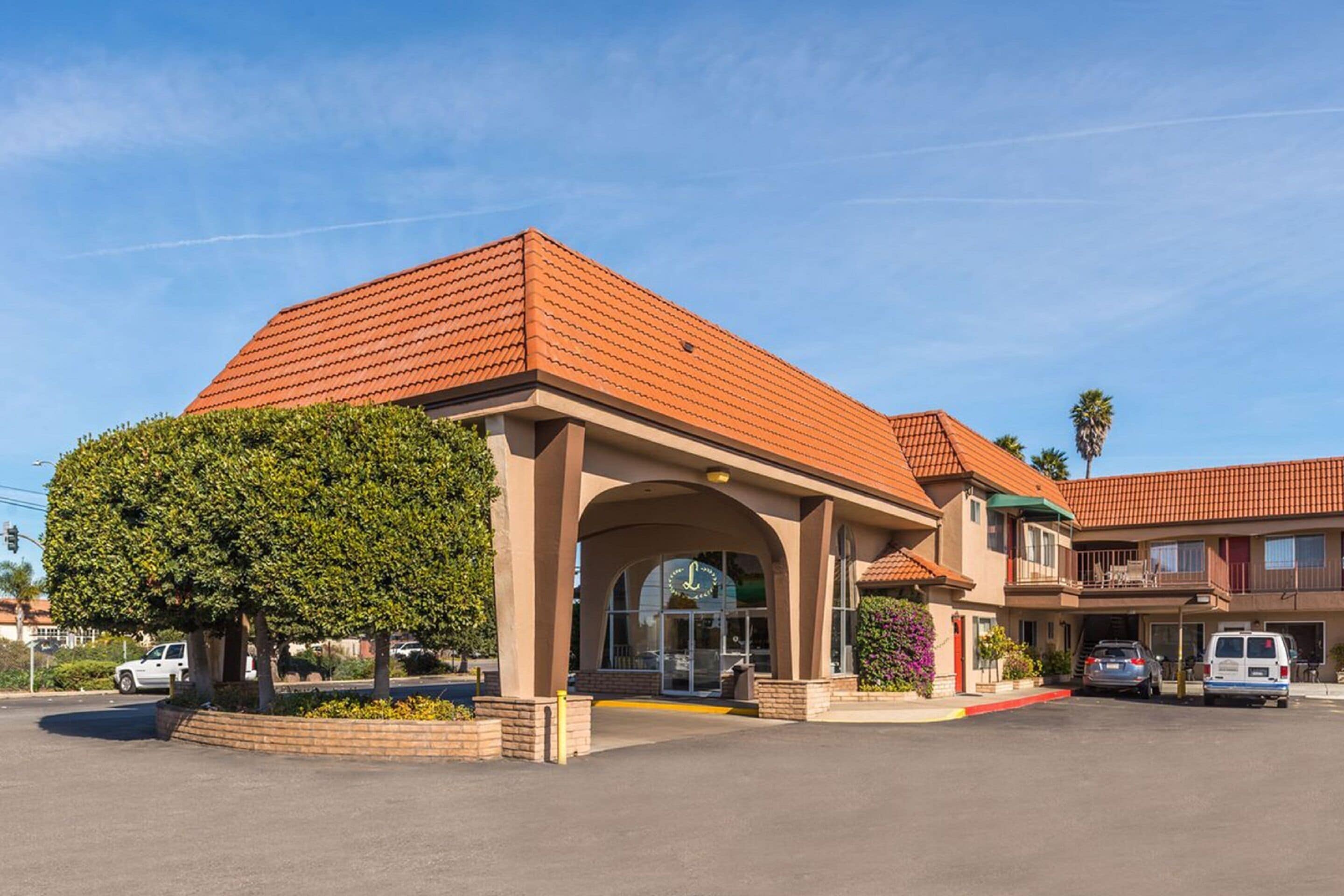 A two-story building with a red-tiled roof, a covered entrance, and a parking lot.