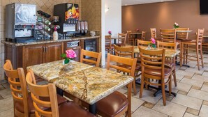 A restaurant with granite tables and wooden chairs, a coffee machine, and a trash bin. - Laurel Inn Motel (Salinas)