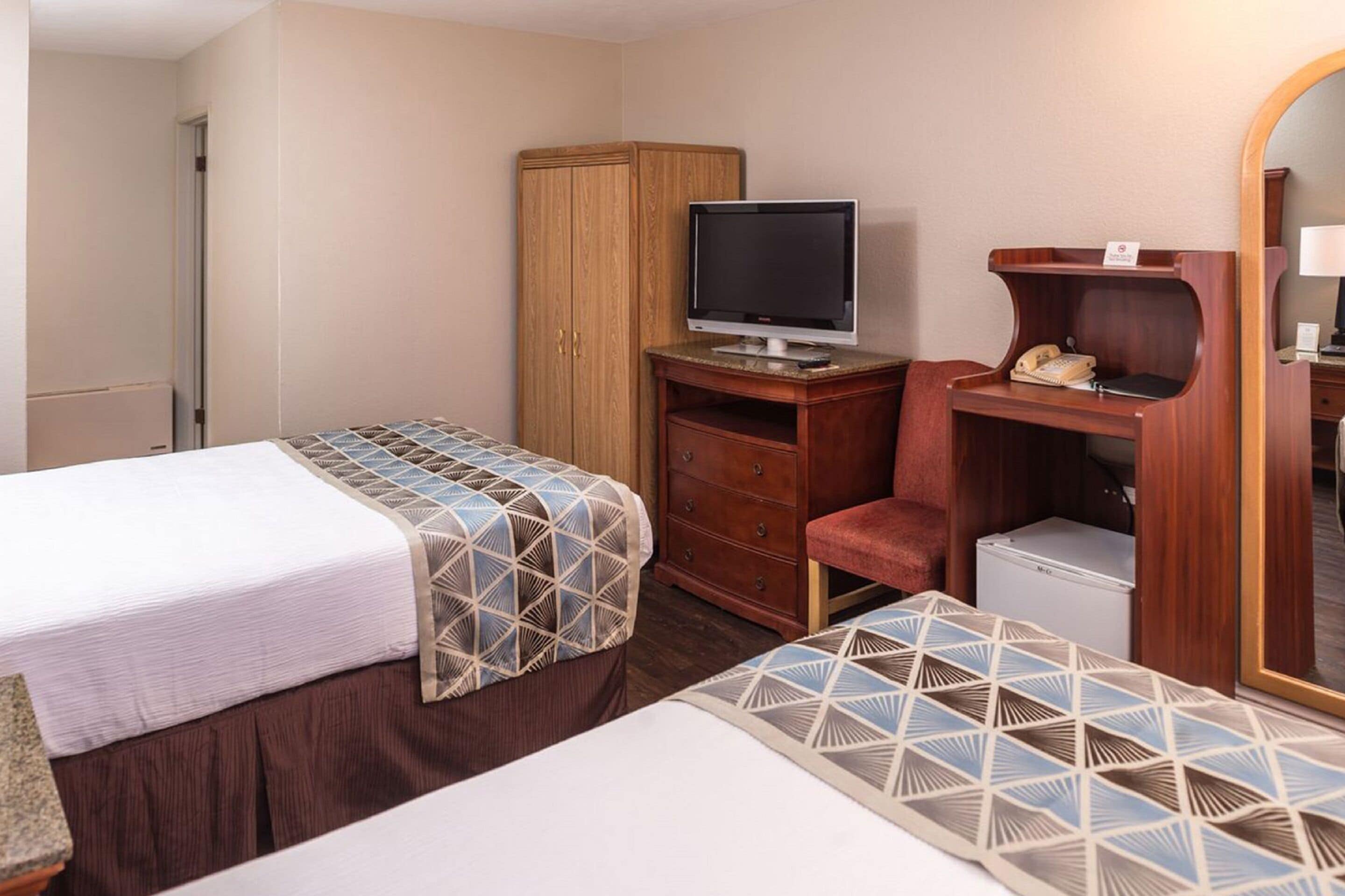 Habitación de hotel con dos camas, un escritorio con computadora, teléfono y armario.
