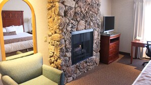 A hotel room with a stone wall, a fireplace, a bed, a TV, and a desk. - Laurel Inn Motel (Salinas)