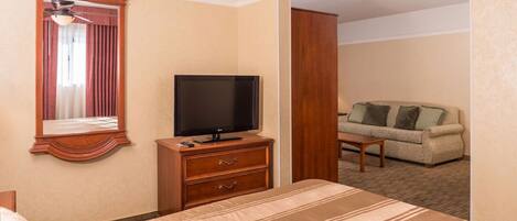 A hotel room with a bed, a television on a wooden dresser, a sofa, and a mirror.