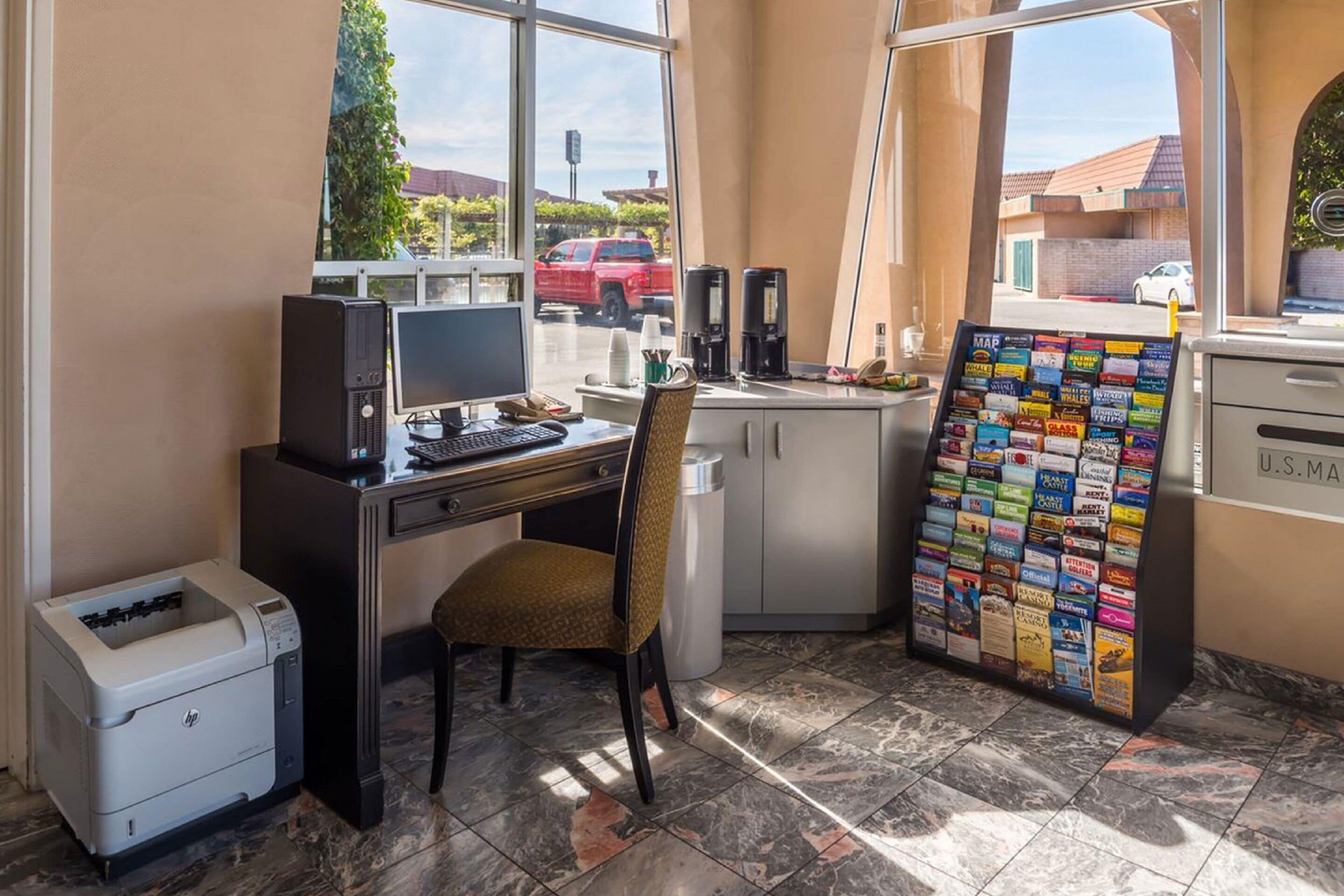 A small office with a desk, computer, printer, and a bulletin board with various papers.