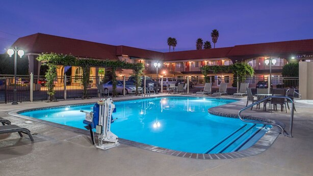 A hotel with a swimming pool, outdoor seating, and a covered area with plants. - Laurel Inn Motel (Salinas)