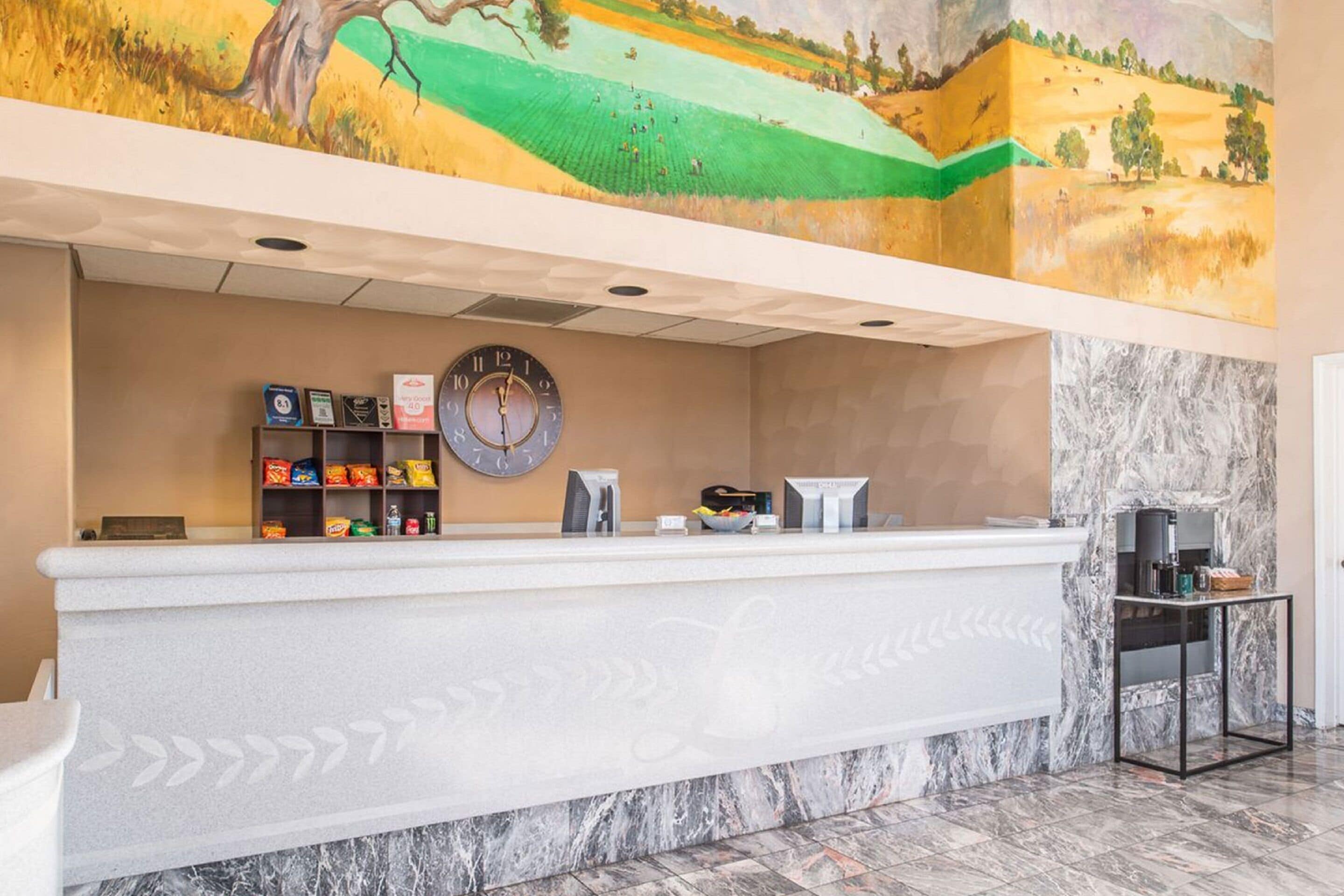 A reception area with a marble counter, a clock, and a mural above.