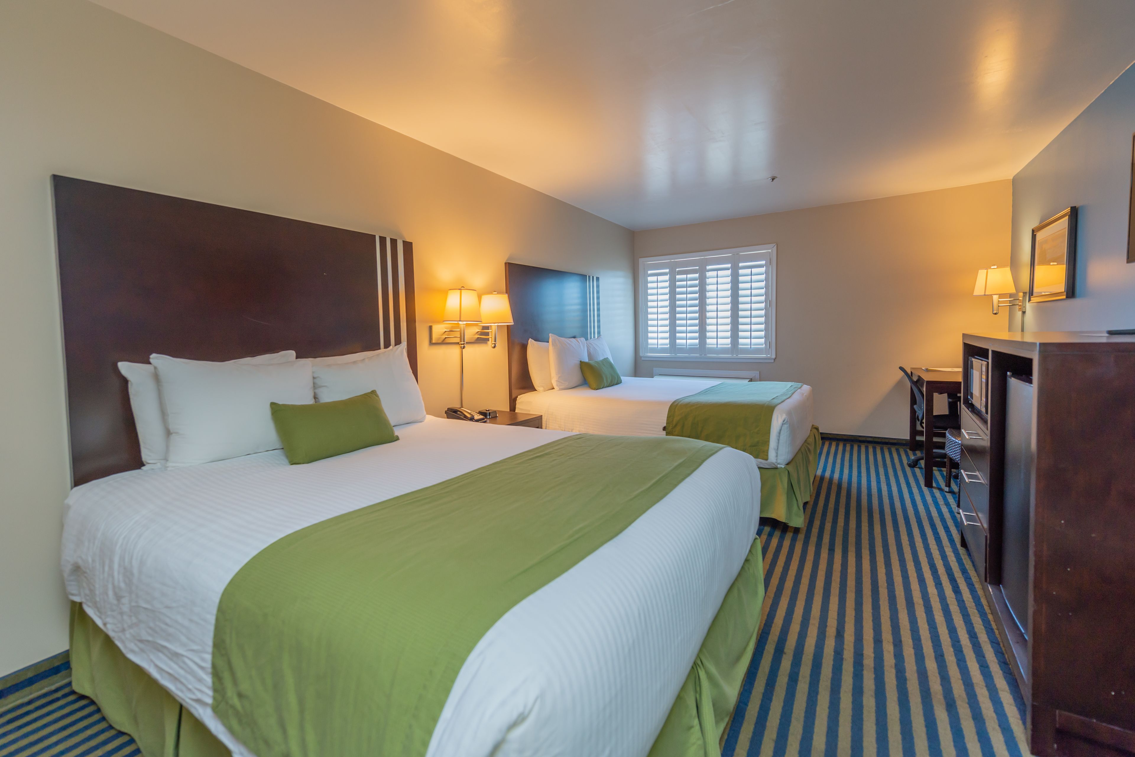 A hotel room with two beds, a desk, and a chair.