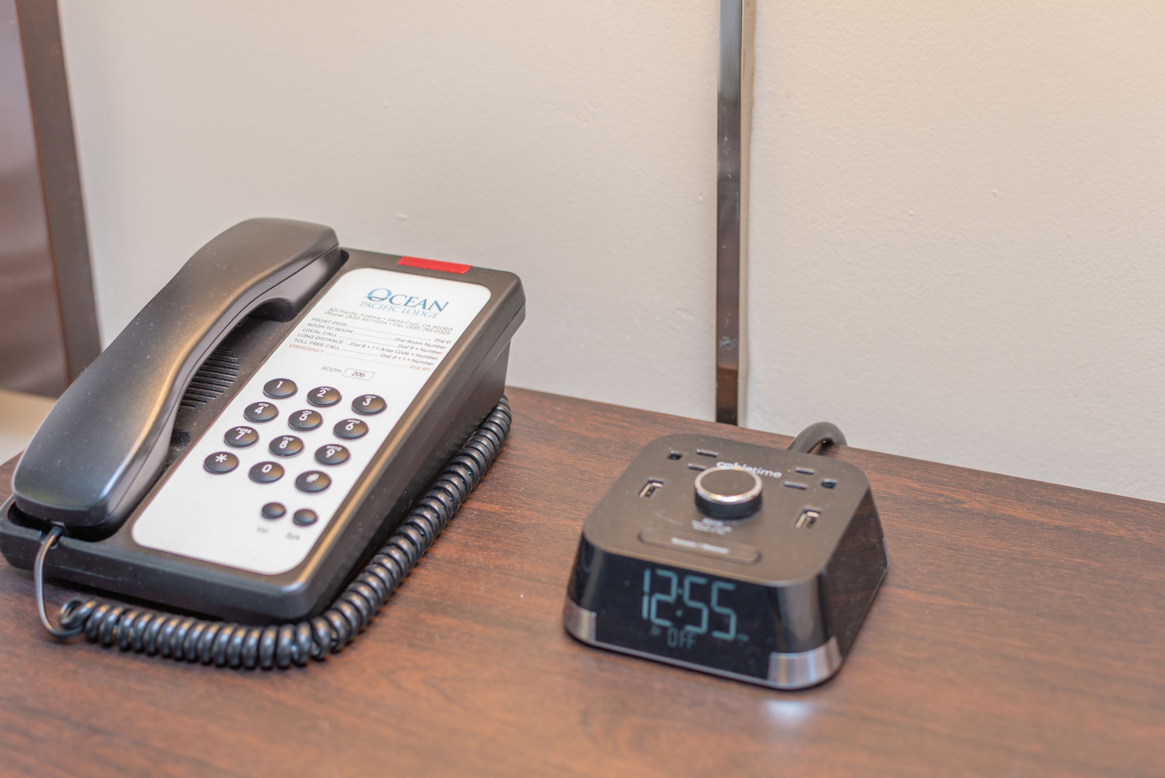 A black telephone and a digital clock on a wooden surface.