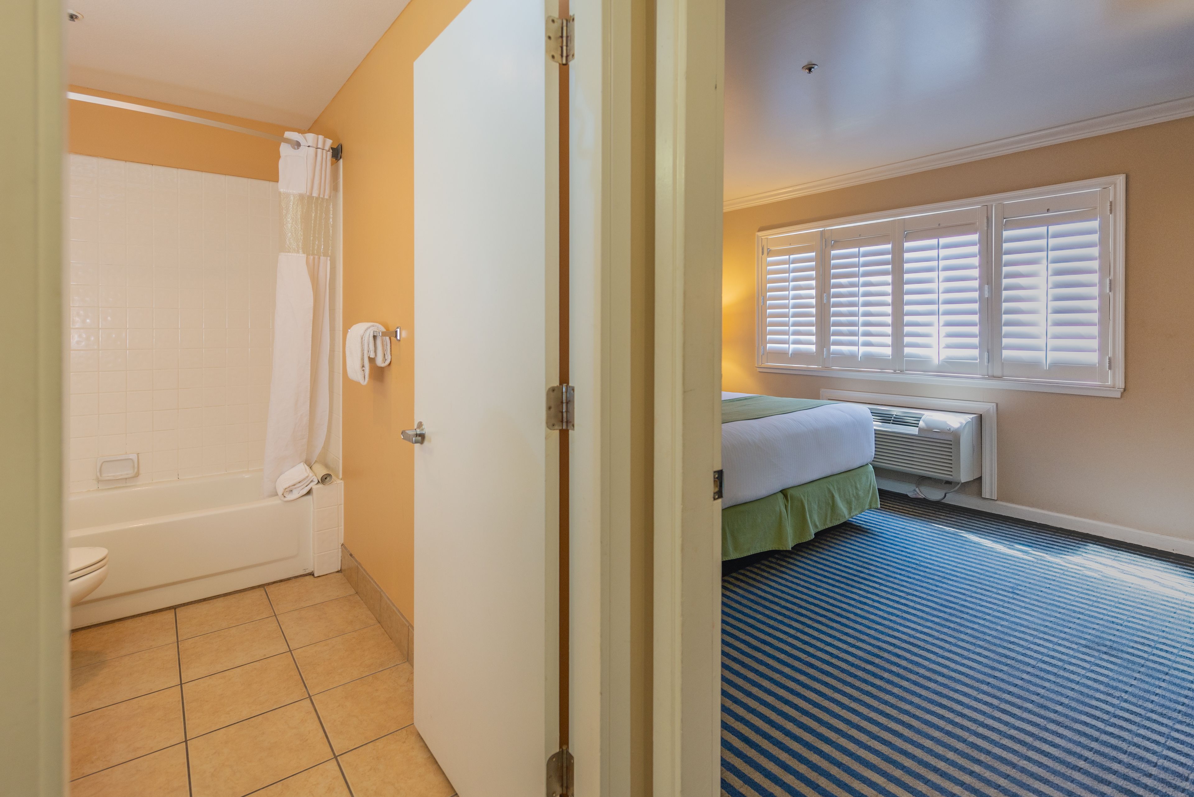 Quarto de hotel com banheiro, cama e janela com persianas.