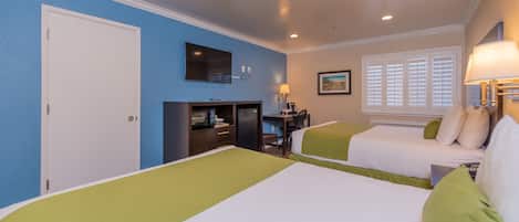 A hotel room with two beds, a desk, a TV, and a window with blinds.