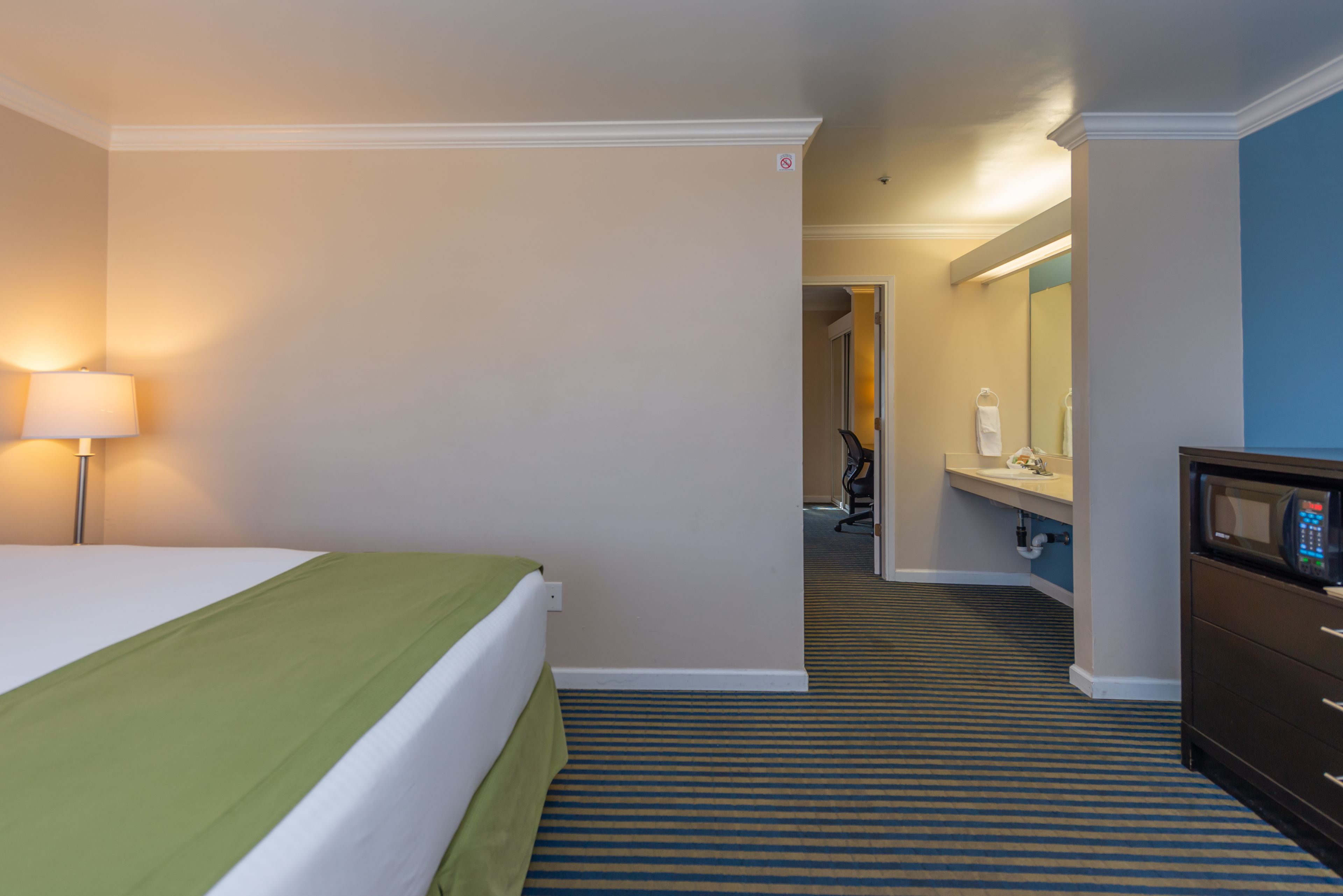 Une chambre d’hôtel avec un lit, une lampe, un four à micro-ondes et une salle de bain visible à travers une porte ouverte.