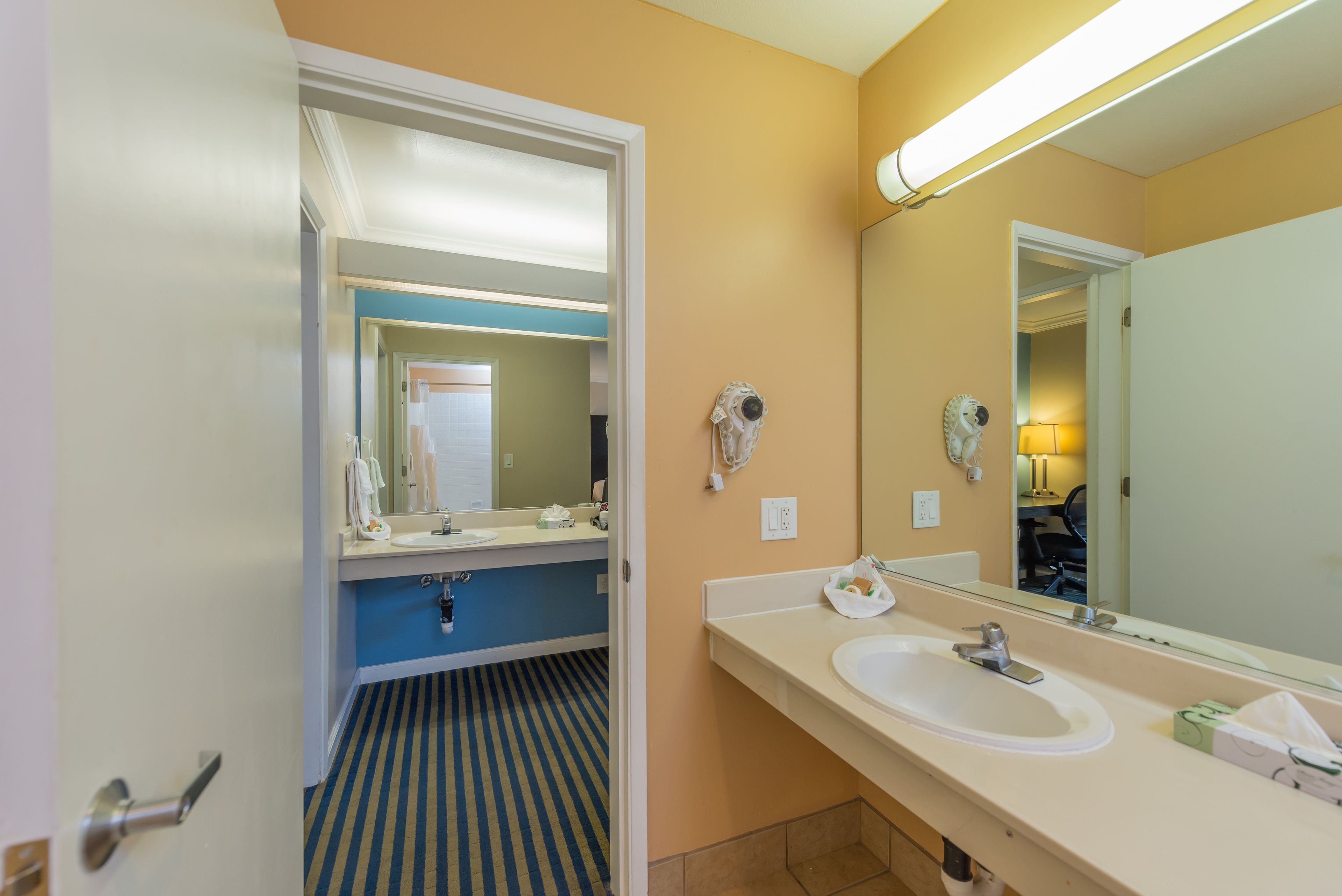 A hotel bathroom with a large mirror, a sink, and a striped floor.