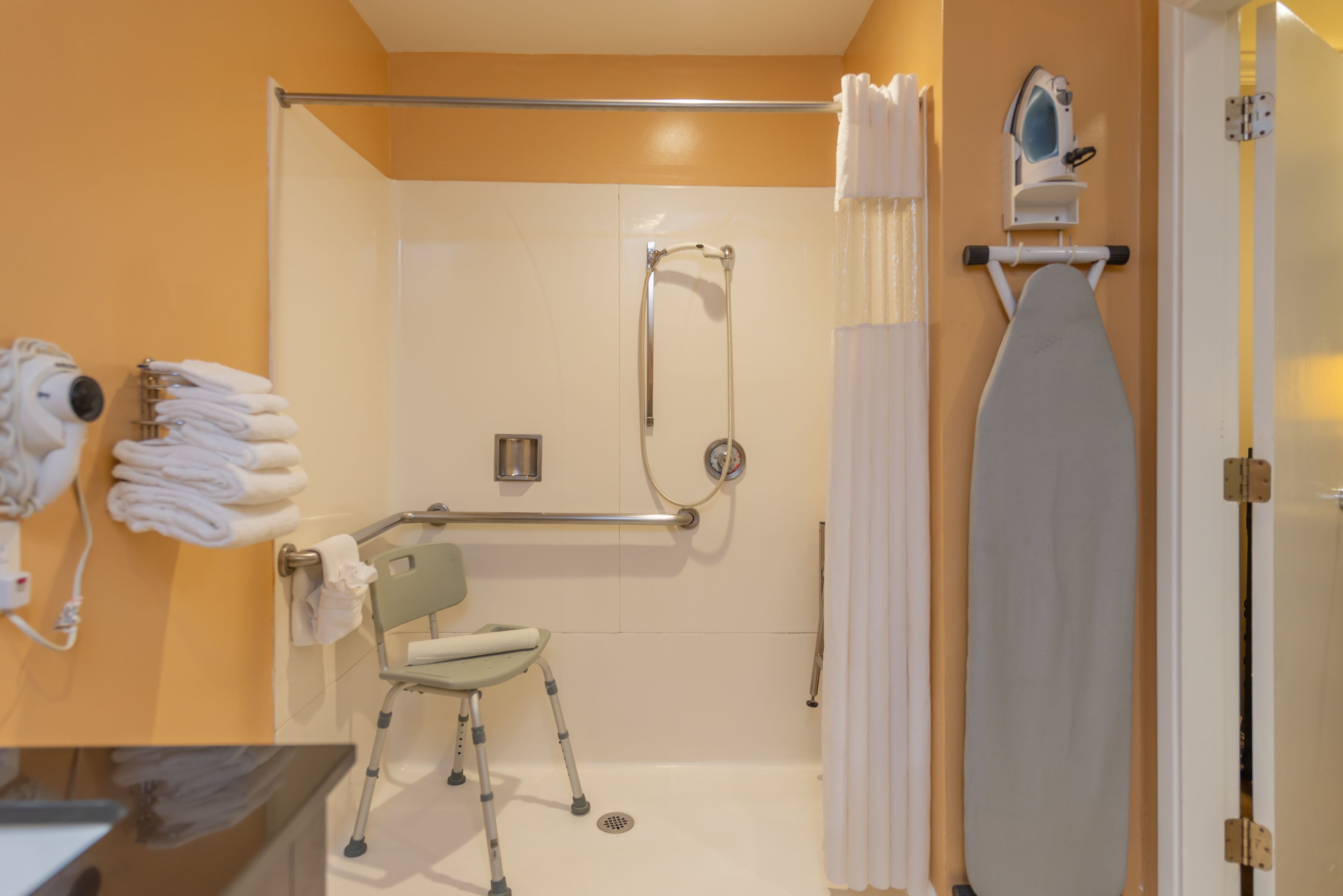 A bathroom with a shower, a wheelchair, a towel rack, and a mirror.