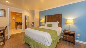 A hotel room with a large bed, bedside tables, a desk, and a bathroom visible through an open door. - Ocean Pacific Lodge (Santa Cruz)