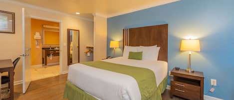 A hotel room with a large bed, bedside tables, a desk, and a bathroom visible through an open door.