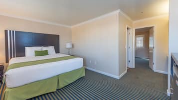 Una habitación de hotel con una cama grande, un cojín verde decorativo, una lámpara de noche y una alfombra a rayas.