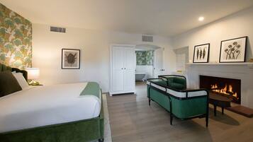 A bedroom with a bed, a green armchair, a fireplace, and a door leading to another room.