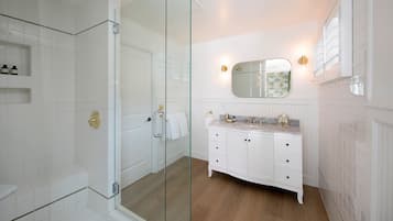 Een badkamer met een glazen douchecabine, witte kastjes en een marmeren aanrechtblad.