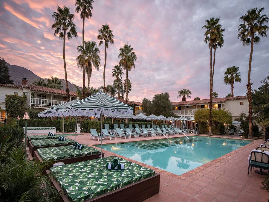 Área de piscina do resort, com espreguiçadeiras e guarda-sóis, cercada por palmeiras e um pano de fundo montanhoso.