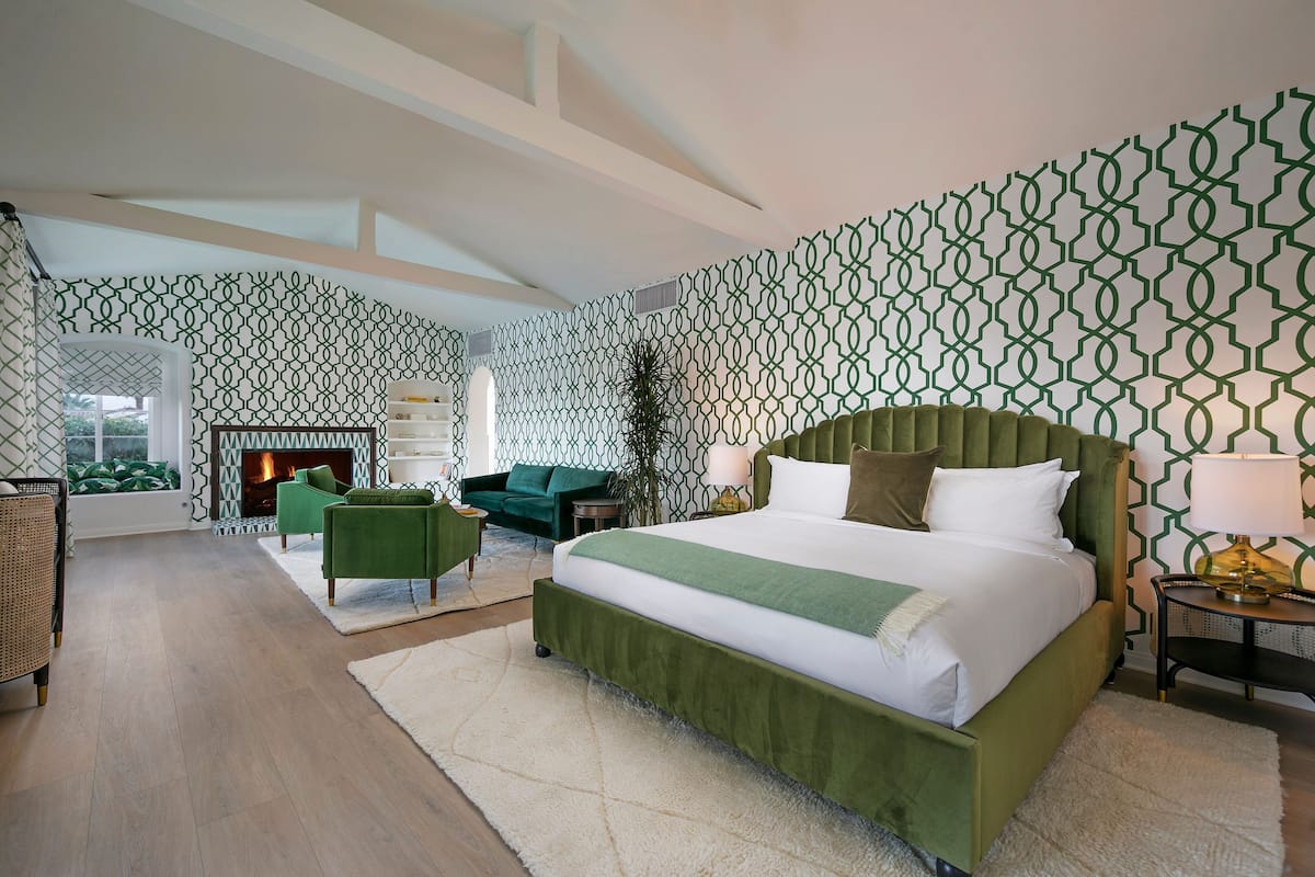 Un dormitorio amplio con una cama grande, cabecero tapizado en verde y papel pintado estampado.