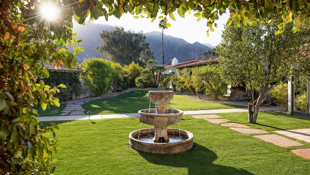 Un jardín bien cuidado con una fuente central, rodeado de césped impecable y senderos.