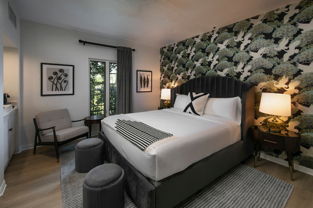 Un dormitorio moderno con una cama grande, dos mesitas de noche con lámparas, una silla y una ventana con cortinas.
