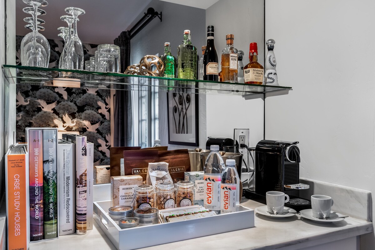 Een barruimte met drankflessen op planken, een koffieapparaat en een schaal met snacks.