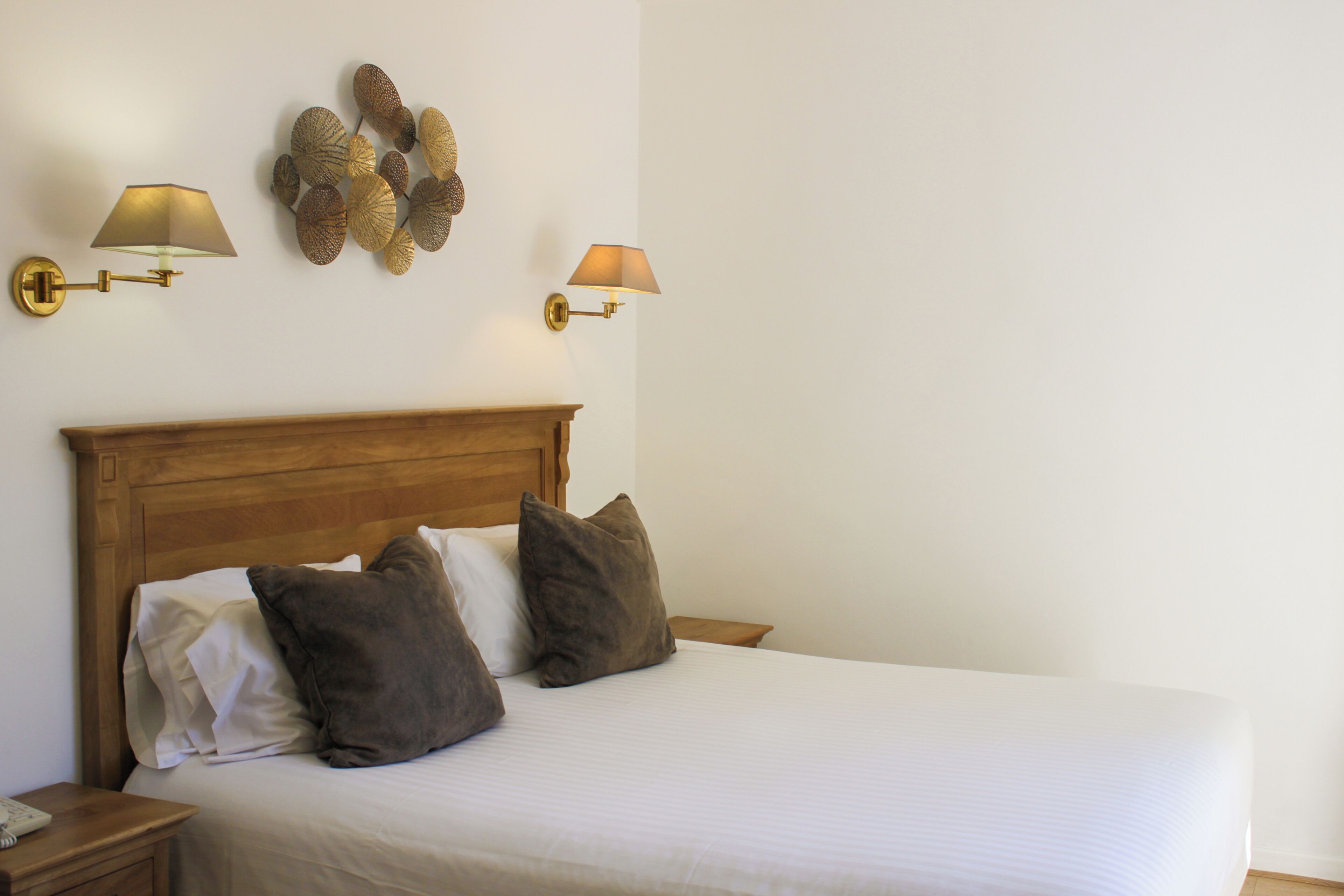 A neatly made bed with a wooden headboard, two bedside lamps, and a decorative wall piece.