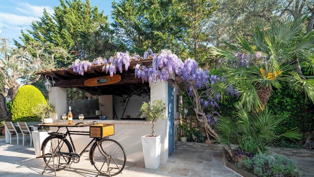 A covered outdoor seating area with a bicycle, a table with a bottle and glasses, and lush greenery. - Hôtel Beau Site - Cap d'Antibes (Antibes)