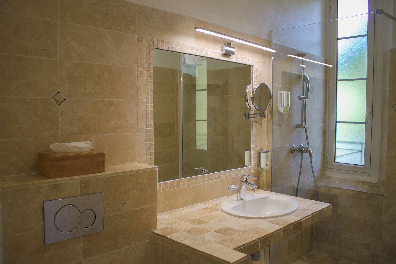 A bathroom with a large mirror, a sink, a shower, and a window.