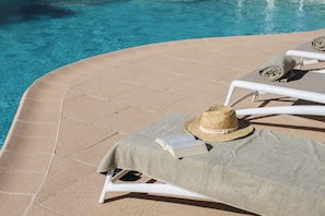 Un espace aménagé au bord de la piscine, avec des chaises longues, un parasol et un chapeau de paille.