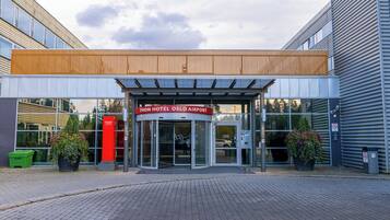 La entrada del Hotel Thon Oslo Aeropuerto, con un diseño moderno, puertas de vidrio y plantas en macetas.