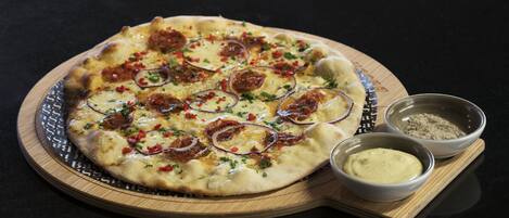 A pizza on a wooden board with two small bowls of dipping sauces.
