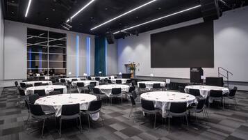 A conference room with multiple round tables, black chairs, and a large screen.