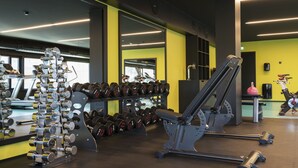 Une salle de sport équipée de matériel d’exercice, d’un tapis de course et d’un miroir qui reflète le matériel.
